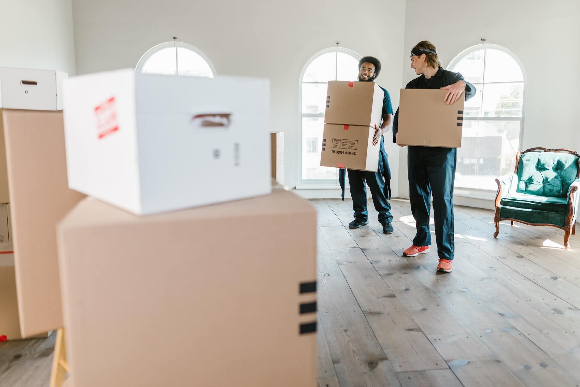 Two people from a removal company carry cardboard boxes out of a flat